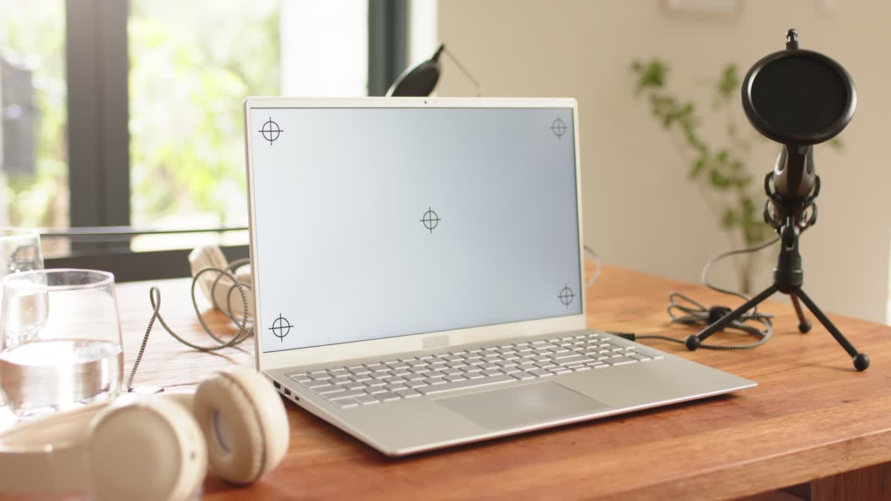 Kamera zoomer ind på laptopskærm nær vindue, mens hovedtelefoner og øretelefoner bevæger sig ud af billedet