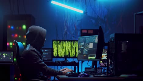 side view on the male software developer in hood working over hacking codes and data at the computer at night