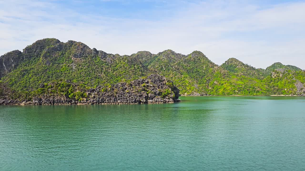 Emerald waters of Ha Long Bay stretch serenely beneath dramatic limestone karsts covered in lush vegetation, creating a mesmerizing seascape where rugged cliffs meet tranquil waters