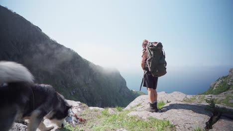 male hiker stops on rocky ledge takes off backpack at mount donnamannen, nordland, norway