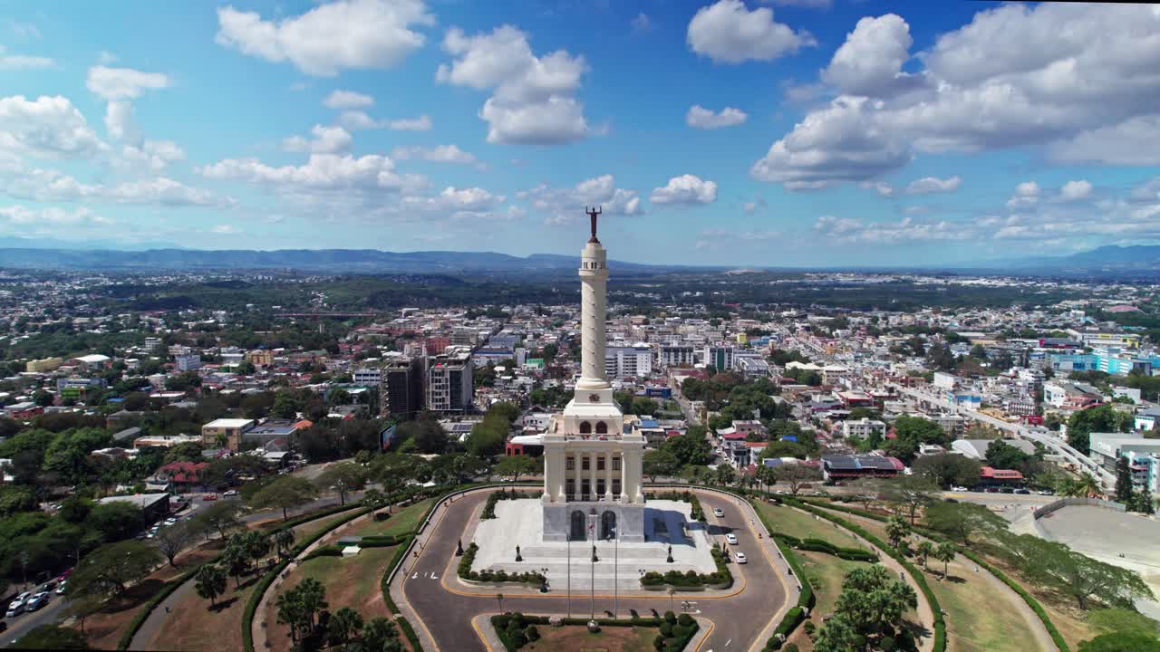 Vista aérea do Monumento aos Heróis da Restauração em Santiago. Ascensão vertical de drone mostrando jardins simétricos, panorama da cidade e céu azul nublado.