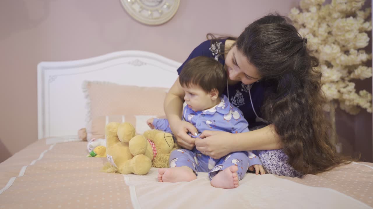 una madre vistiendo a su bebé en la cama.