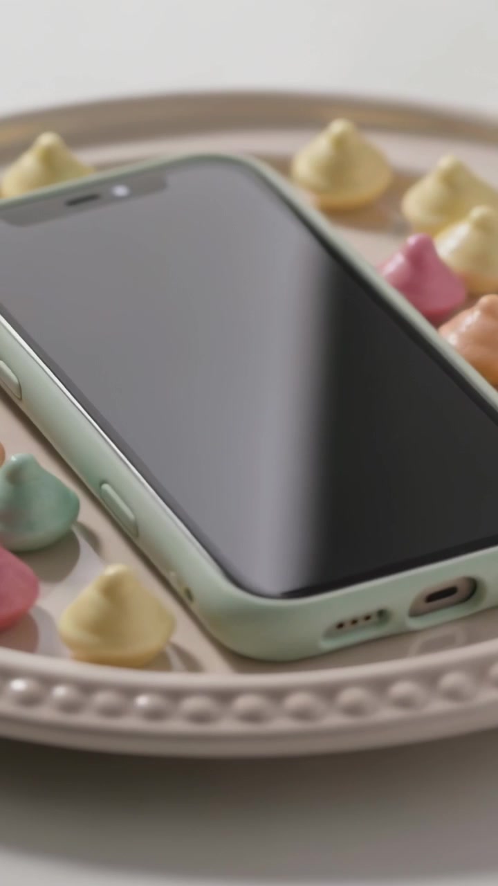 Vertical video: Shifting camera showing mint phone on plate with pastel candies in studio