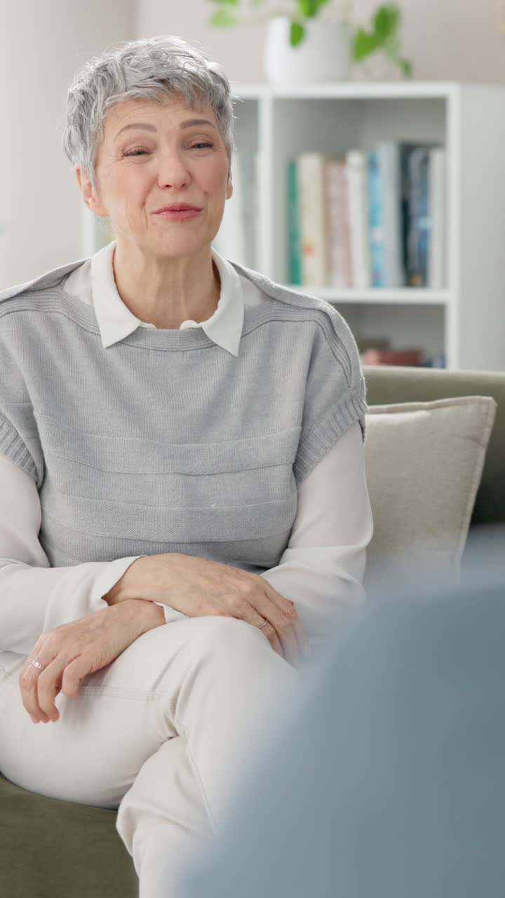 En kvinde smiler og taler med en anden person, mens hun sidder på en sofa