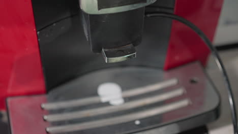 close-up shot of espresso machine nozzle, focused on metal spout releasing a small droplet of coffee into a silver tray below. modern kitchen appliance in action with shiny surface and chrome finish