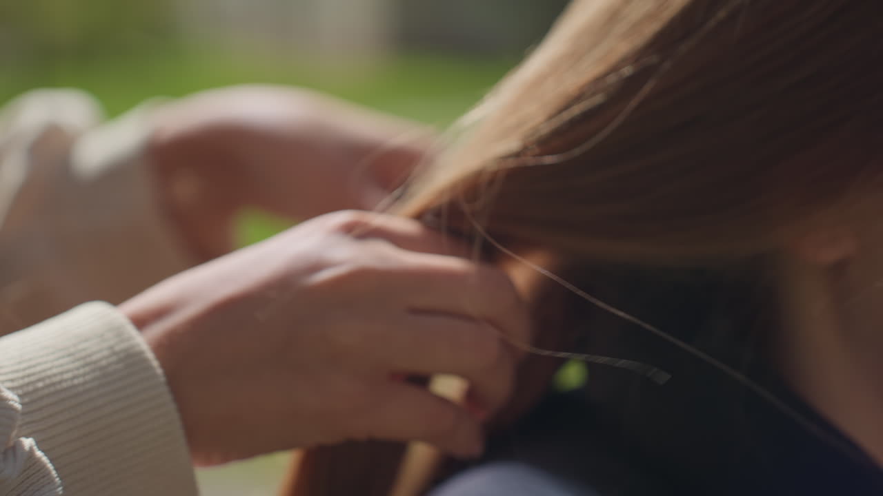 능숙한 머리 땋기, 젊은 스타일리스트가 머리를 조심스럽게 만지고, 햇빛이 비치는 장면에서 꼼꼼한 헤어 스타일링 작업이 포착되었고, 섬세한 손가락이 평화로운 햇빛 아래에서 머리카락을 엮고 있어요.