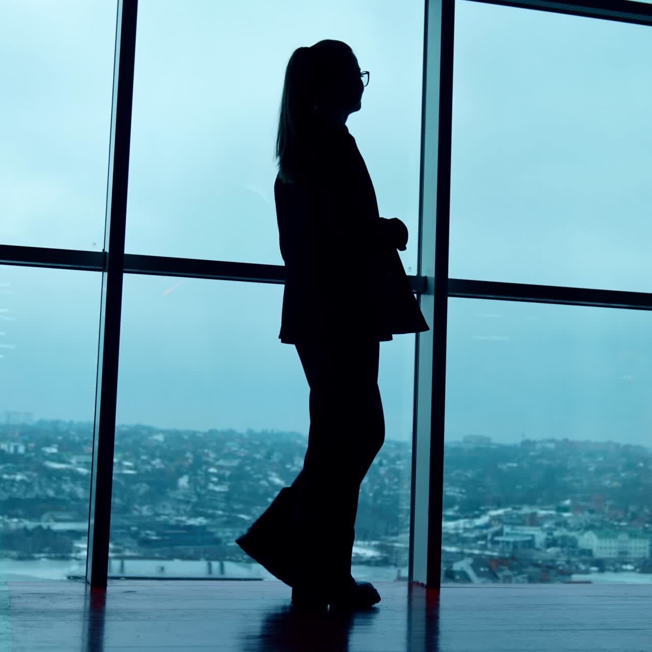 Mujer con traje holgado camina junto a las ventanas panorámicas de la oficina. Silueta de empleada. Vista de ángulo bajo