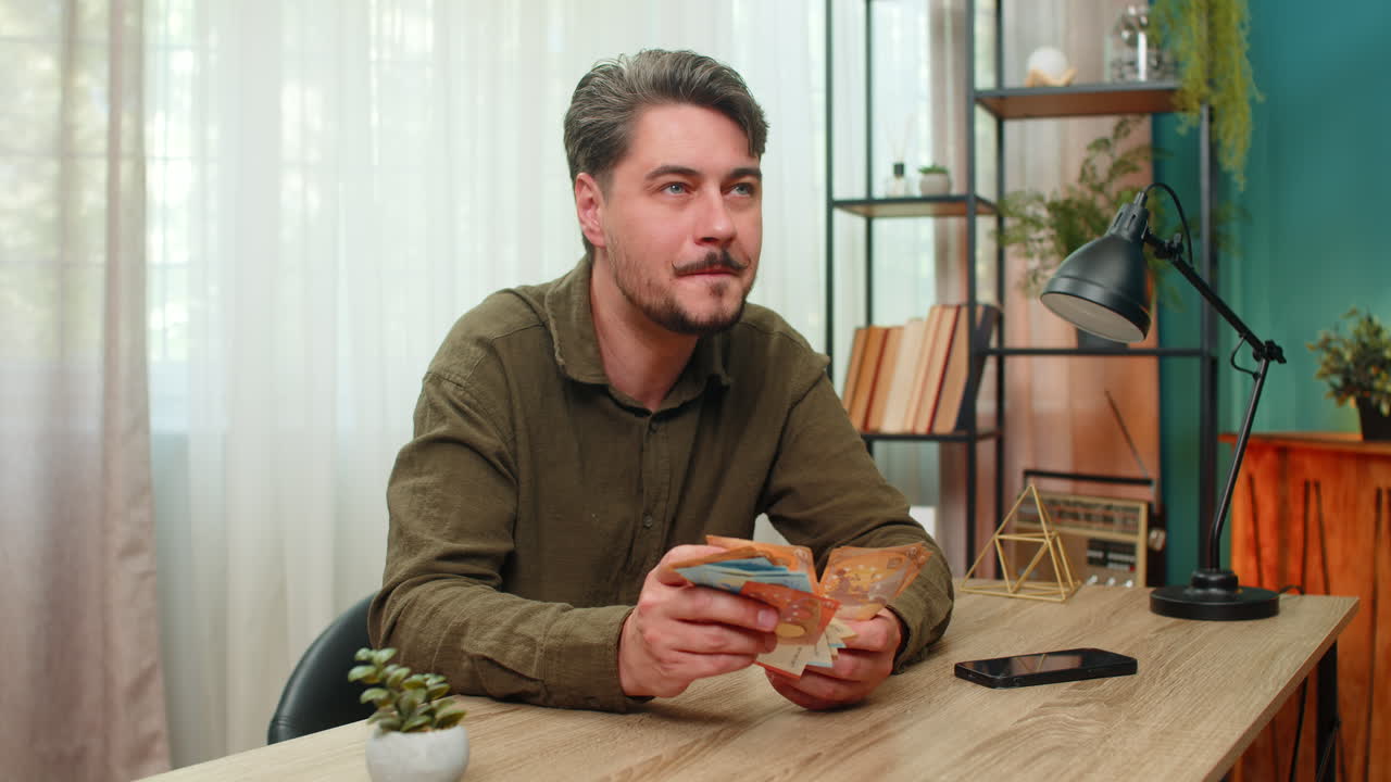 Middleaged man counts cash smiling showing big financial success euro bills wealth at table desk