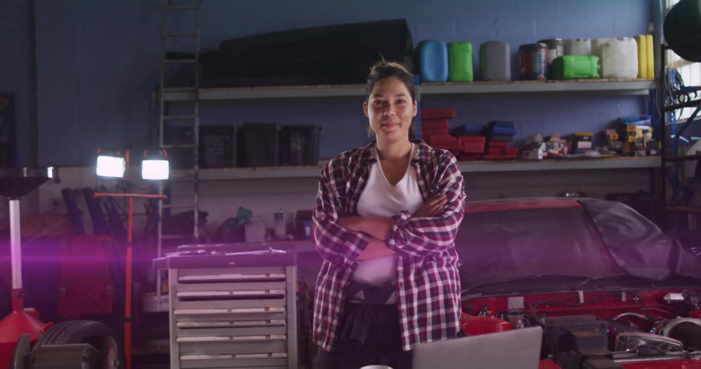 Una meccanica che aggiusta la postura mentre una striscia al neon attraversa l'inquadratura in un'officina, evidenziando gli attrezzi.