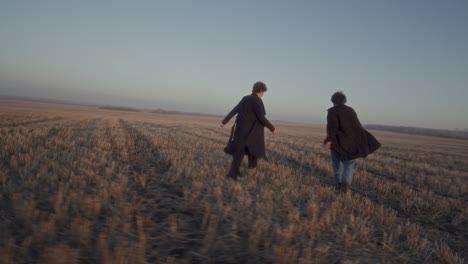couple running, laughing and playing together in field during sunset