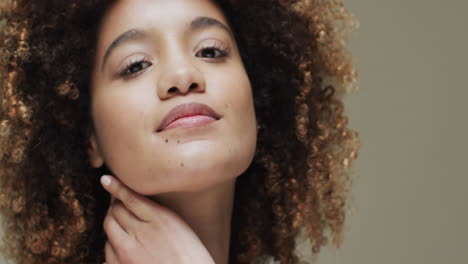 mujer biracial con cabello oscuro tocando el cuello sobre un fondo beige, cámara lenta
