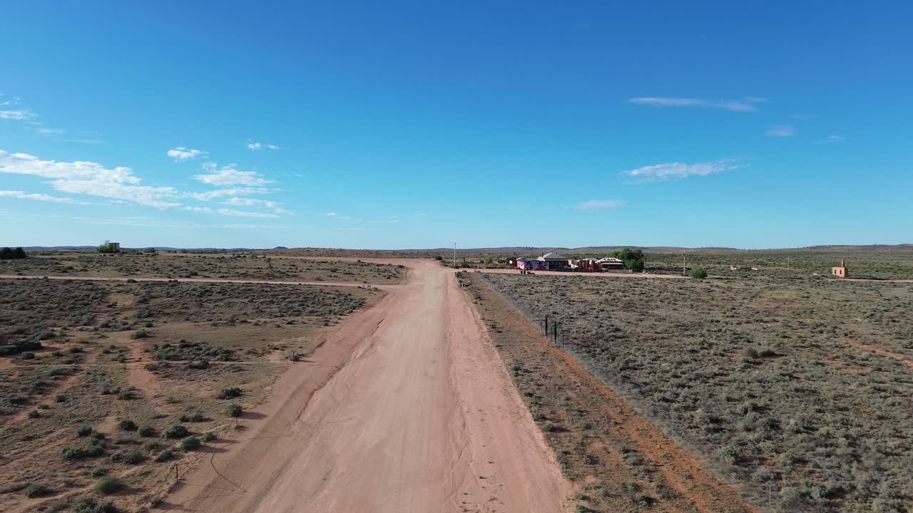 Drone footage captures a rugged dirt road in Silverton, Australia, winding through vast red-earth desert, sparse bushland, and endless horizons, showcasing the raw beauty of the outback wilderness.