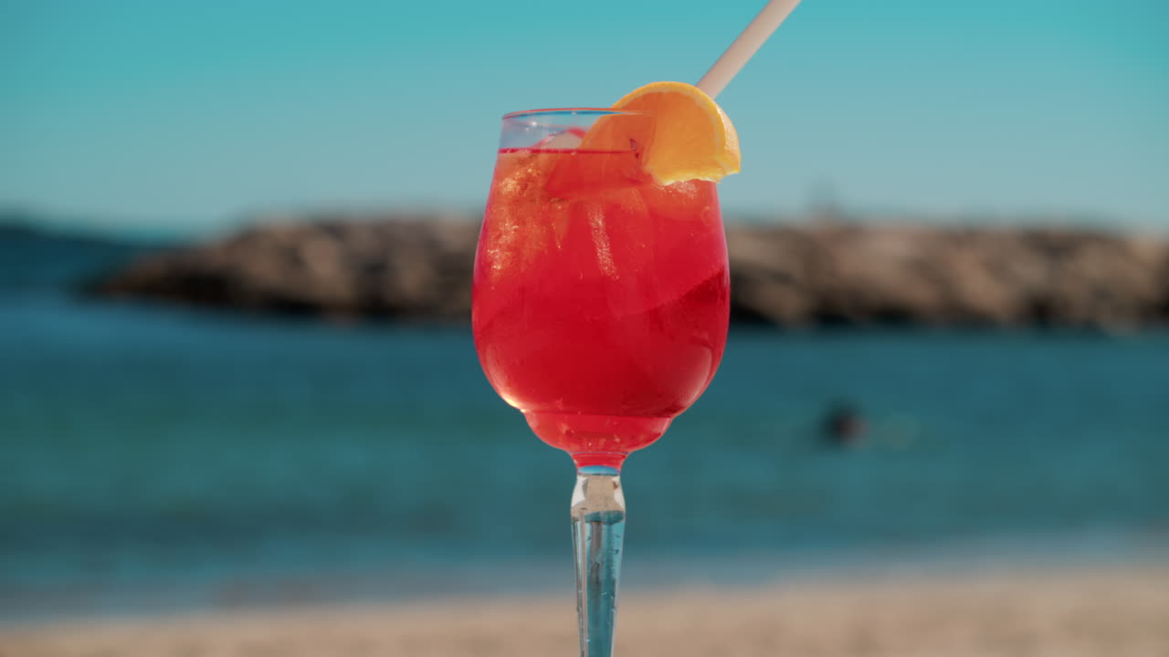 Un cocktail rinfrescante rosso-arancio con ghiaccio e fetta d'arancia sullo sfondo del blu intenso del Mar Mediterraneo