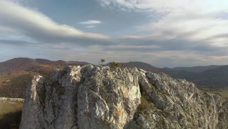 tracking aerial shot over rocky hill, mountain and forest as background