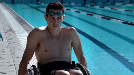 a male swimmer in goggles by a bright blue swimming pool, featuring a wheelchair user