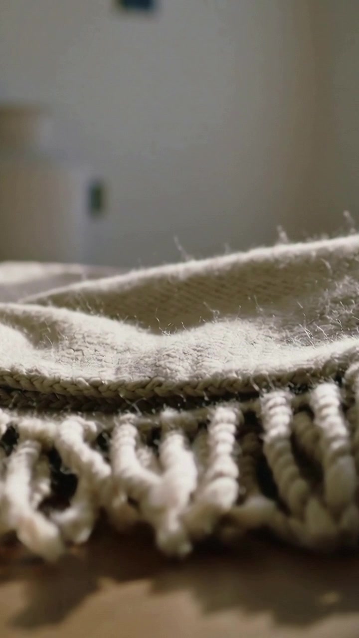Video verticale: Fotocamera con messa a fuoco a slitta che mostra la texture di una coperta tessuta color crema su un tavolo a casa