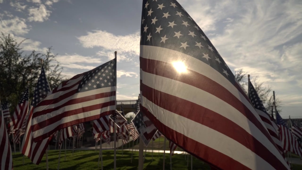 Il sole splende intensamente attraverso il tessuto di una bandiera americana sventolante in un parco commemorativo. Questa ripresa ravvicinata in controluce cattura una mostra orgogliosa e patriottica che onora il Giorno dell'Indipendenza e gli eroi nazionali.