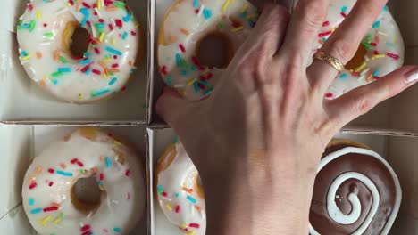 top down shot of a girl picking and then keeping bright and colorful sprinkled donut from a food packet