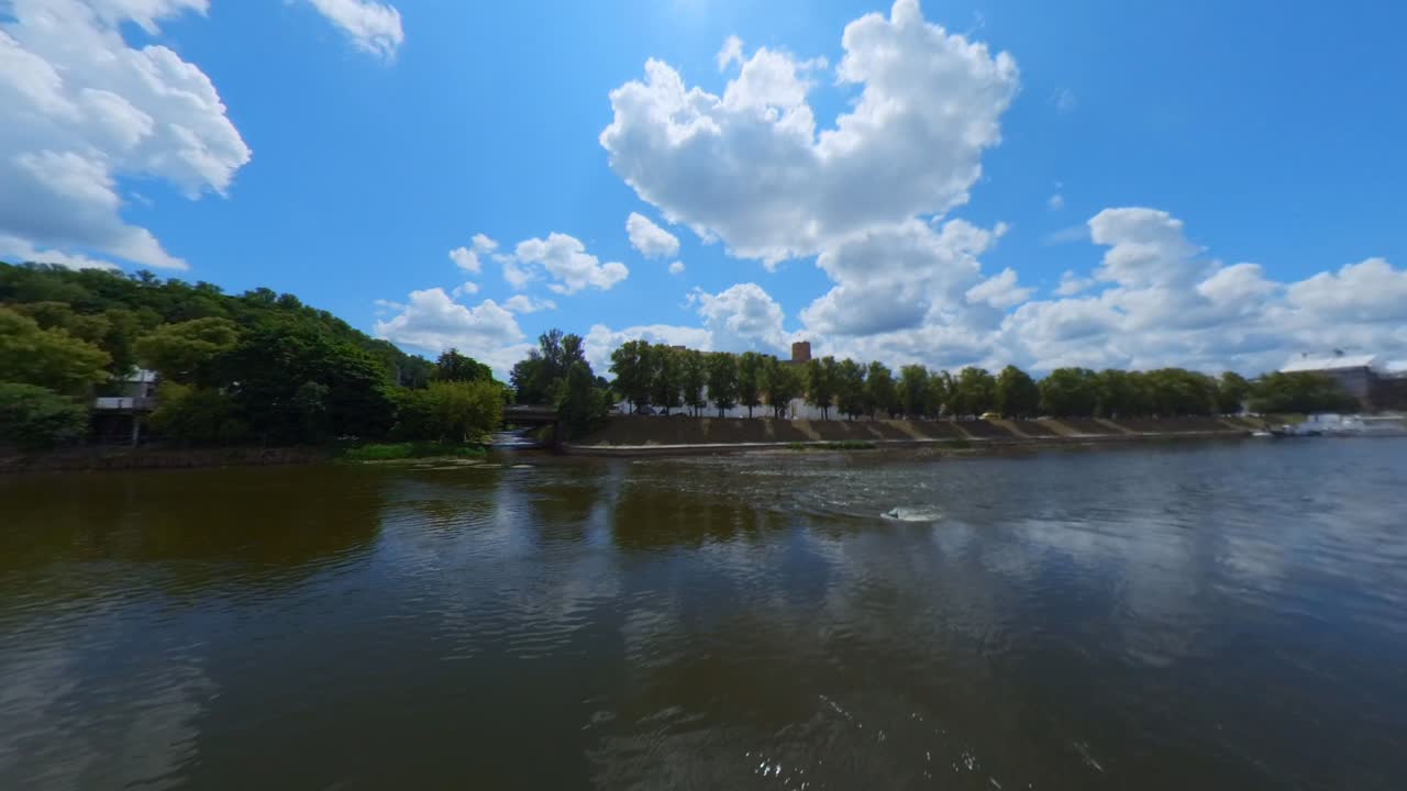 A scenic river landscape under a bright blue sky with white clouds