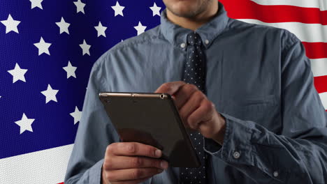 animation of flag of usa over happy caucasian businessman using tablet