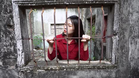 Ethnic-woman-looking-through-window-with-metal-grid-in-old-house