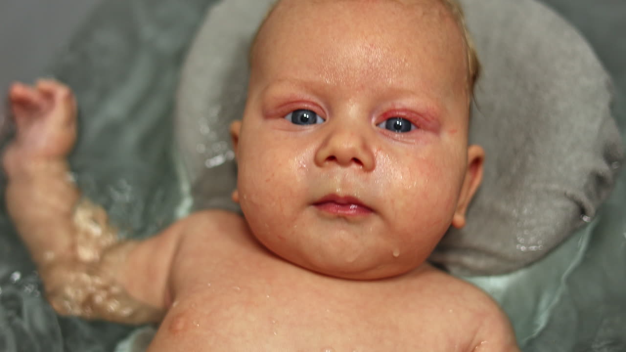 Bathing the baby in the bath while lying on the stand. Baby's first baths. Baby hygiene. A 3-month-old baby is lying in the bathroom