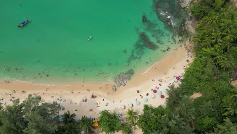 aerial view of surin beach in tropical phuket, thailand, with turquoise waters, swimmers, umbrellas, and lush greenery.