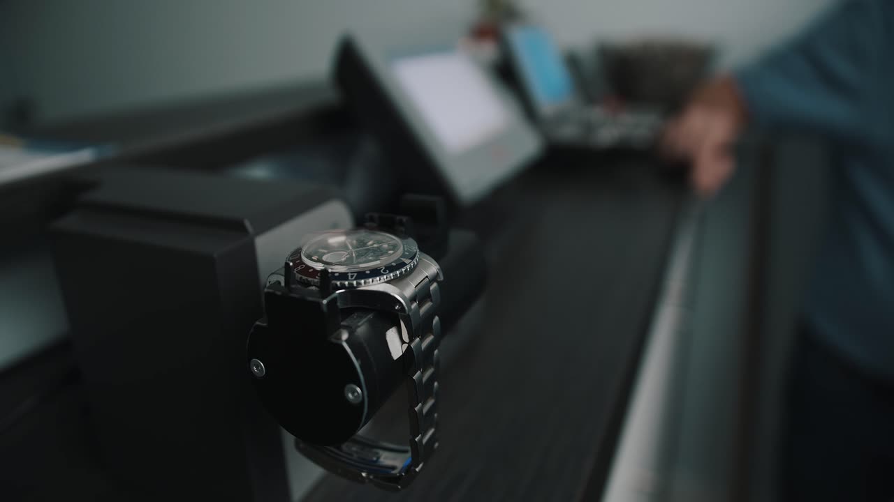 A beautiful metal watch placed on a timegrapher reading cylinder to determine the beat rate of the watch with a watchmaker explaining the details in the background - close up