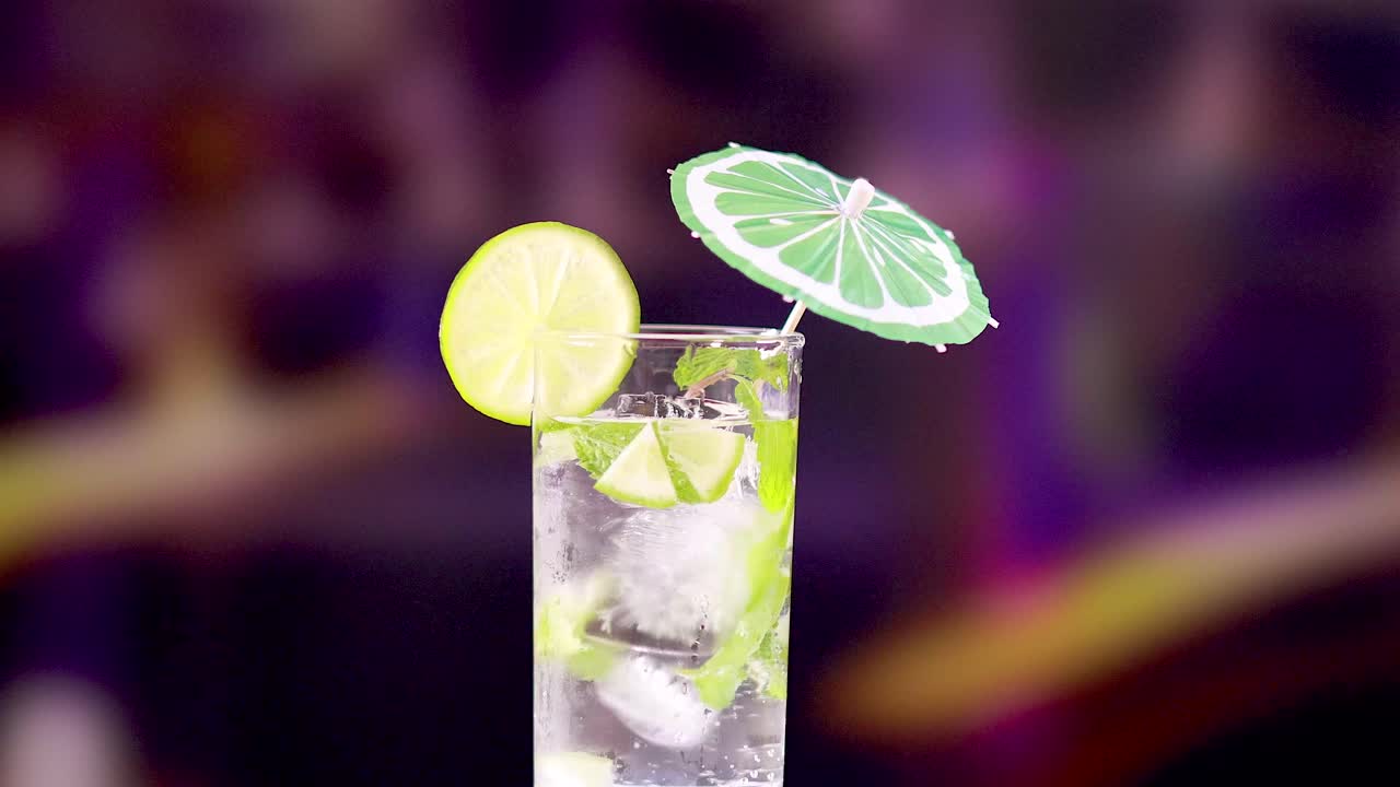 A vibrant mojito cocktail with lime slices and a decorative umbrella, set against a colorful, blurred background