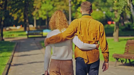 couple walking and hugging along sunny city park with a german shepherd dog