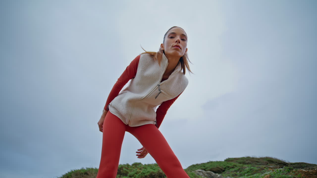 Confident sportswoman looking camera relaxing at cloudy nature after workout