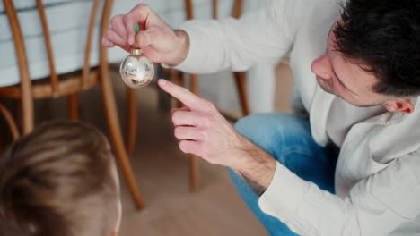 young boy hands dad a christmas bauble in hand