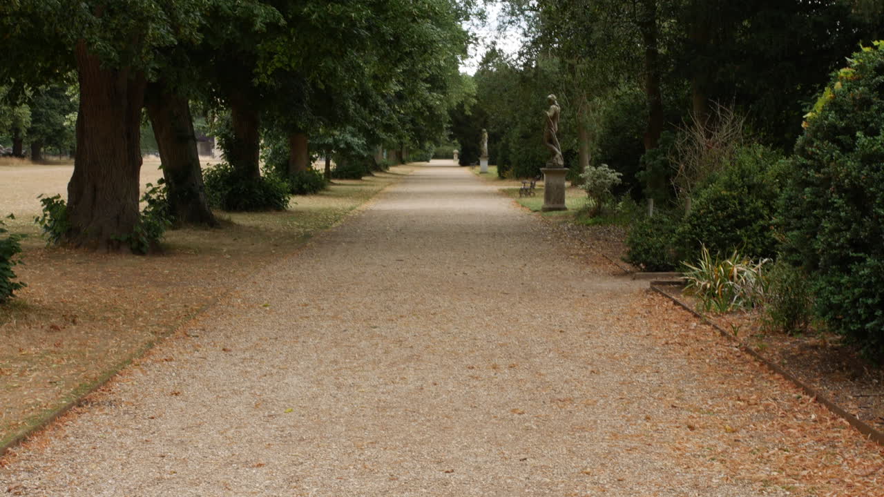 Un viale ghiaioso nei giardini di un palazzo signorile con statue e alberi