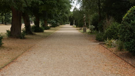 a gravel driveway in the palace mansion gardens with statues and trees