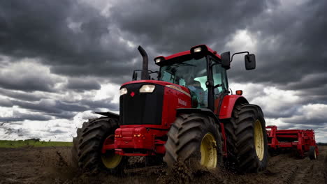 red tractor works in muddy field under overcast sky
