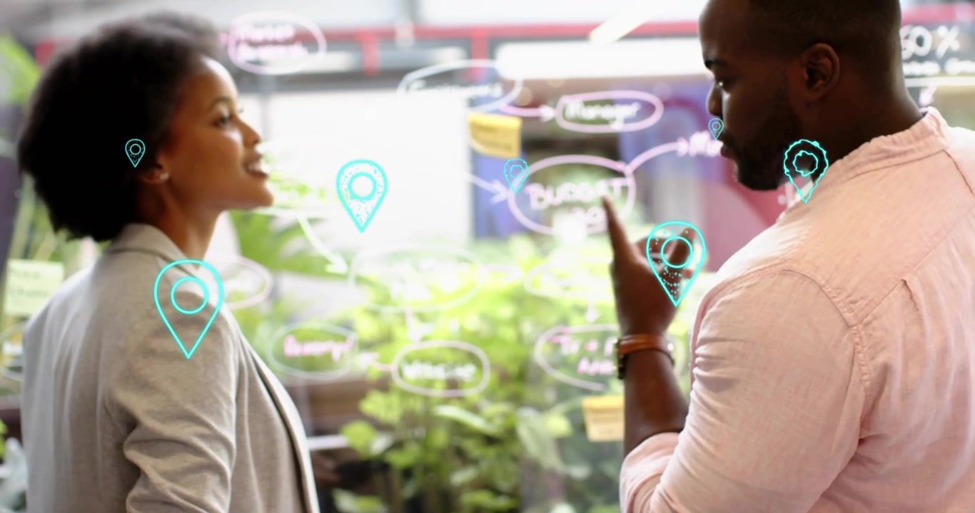 Woman tapping tablet, gesturing at glass board showing icons while man pointing at marketing plan