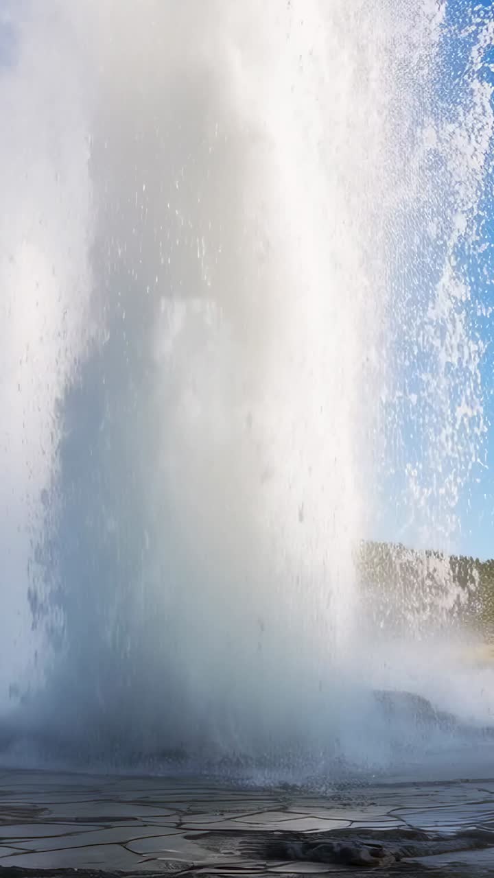 Vídeo vertical: respiradero de géiser que arroja una columna de agua procedente del calor del subsuelo en una cuenca, rociando vapor.