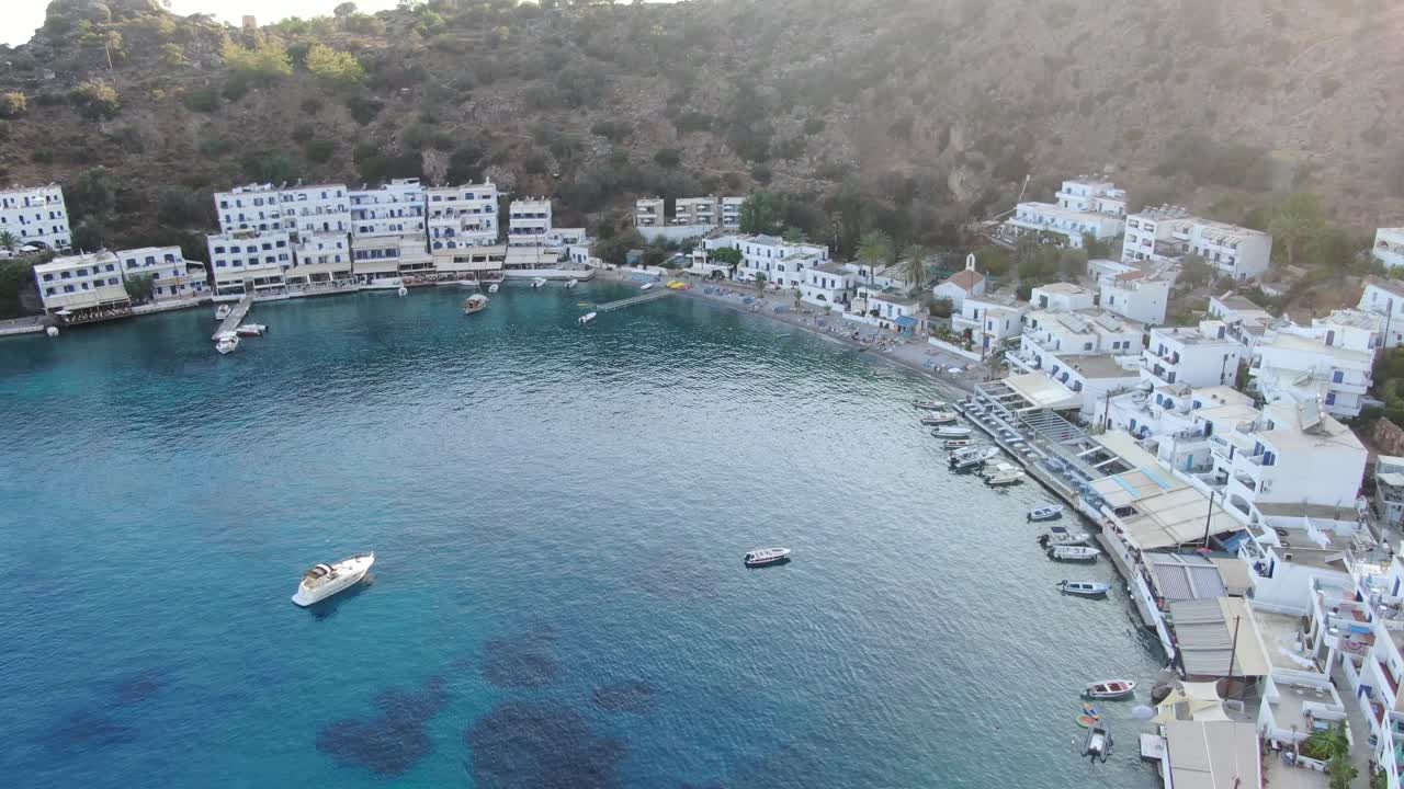 vista de drones en grecia volando sobre el mar azul en loutro pequeña ciudad de casas blancas y pequeños barcos al lado de una colina en un día soleado