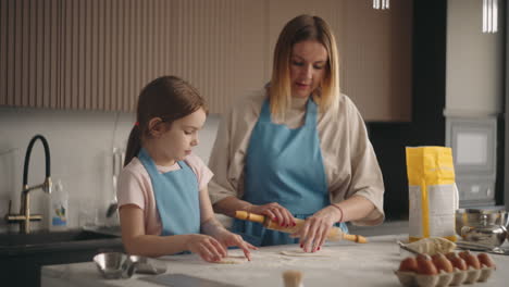 mother and daughter are cooking cake or buns in home kitchen woman is teaching child to cook