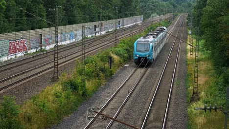 a small blue commuter train with only one car moves down the line of the railroad