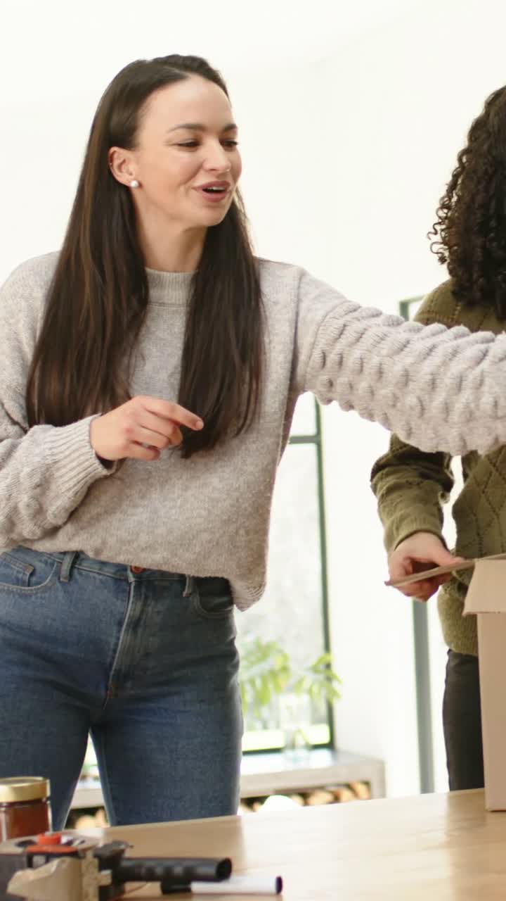 Video verticale: Collaboratore che parla con un maglione grigio, piega un indumento su un tavolo preparando una scatola per donazioni, barattoli.