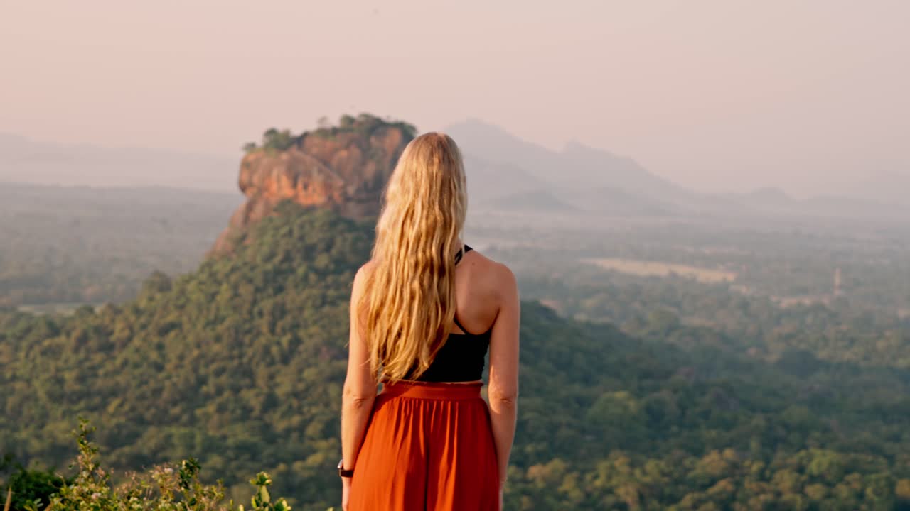A woman admires the majestic Sigiriya Rock as the sun rises over the Sri Lankan jungle. A peaceful and iconic moment in nature, perfect for travel and cultural themes.