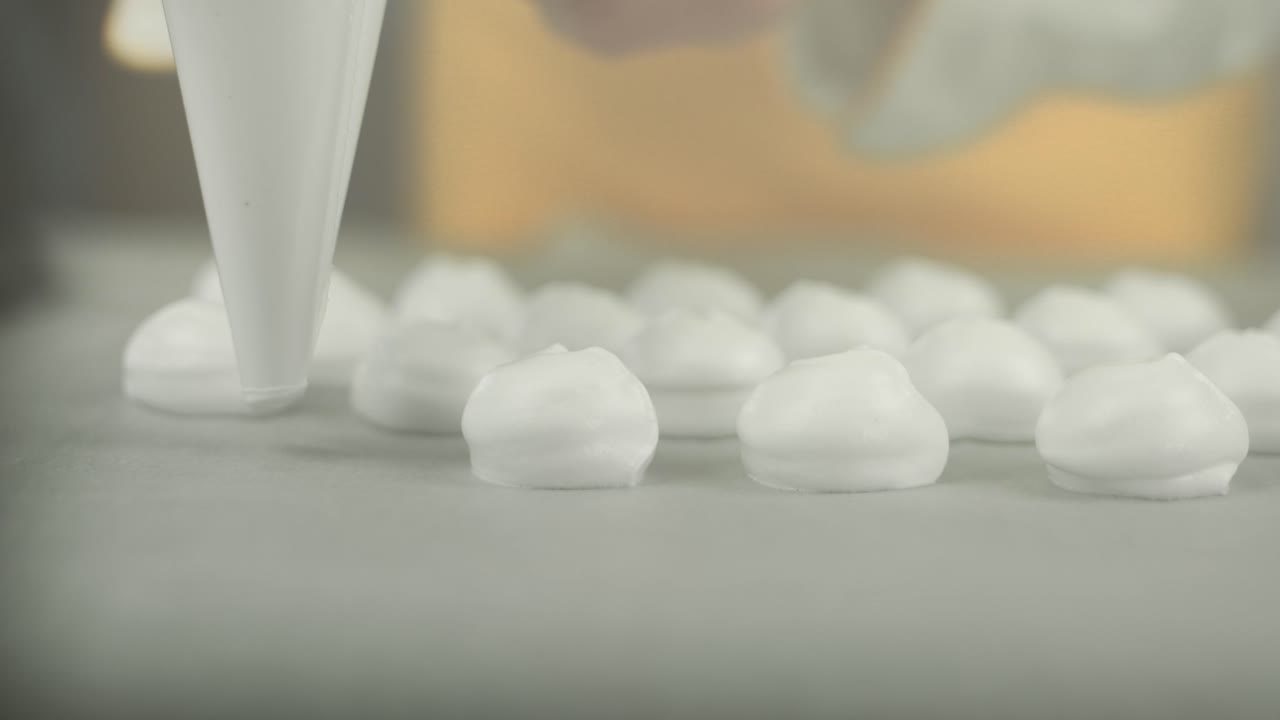 머랭을 만들기 위해 백킹 플레이트에 아이싱 백이 있는 셰프가 휘저은 계란 흰 크림을 닫습니다