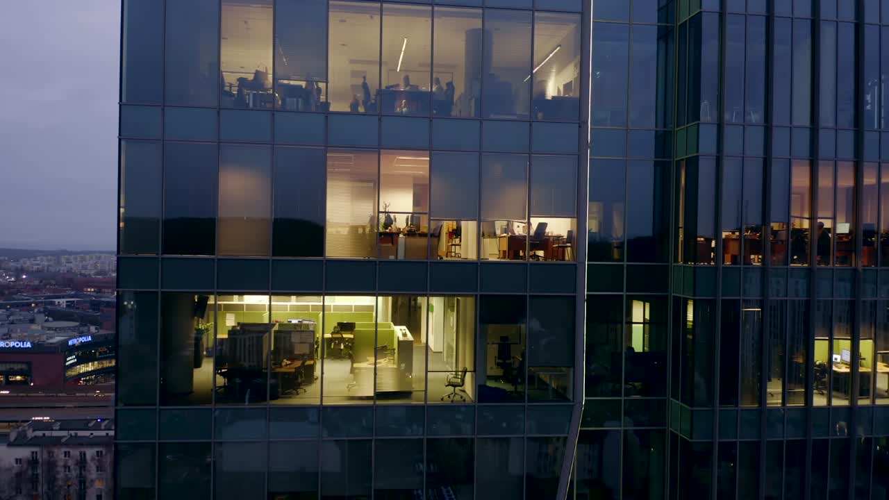 un dron disparó a un rascacielos nocturno con ventanas de oficinas y gente de negocios trabajando hasta tarde en las computadoras.