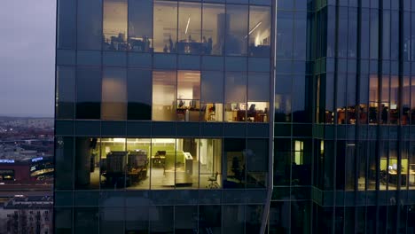 drone shot at a night skyscraper with office windows and business people working late at computers.