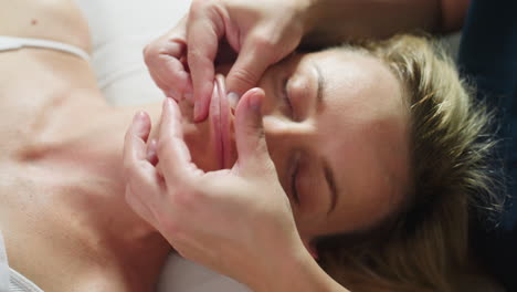 high angle view of therapist gently massaging lips to cheek of relaxed woman on spa bed with closed eyes and relaxed shoulders showcasing soothing facial therapy technique for calm skin rejuvenation