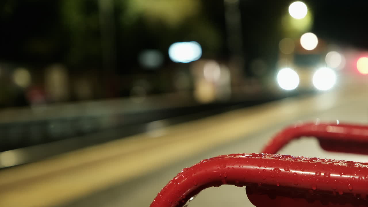 A Northern Rail train arrives at Todmorden Station with the red arm of a wet bench in focus showing large raindrops as the background stays blurred