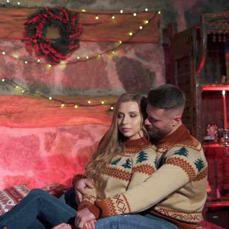 young man and woman on bed at christmas. couple in love in same knitted sweaters and thick socks are sitting on the bed in christmas decorated bedroom.