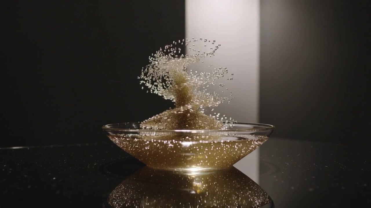 Spirale di liquido dorato che forma una ciotola di vetro in studio dopo un impatto centrale, con goccioline che si alzano retroilluminate.