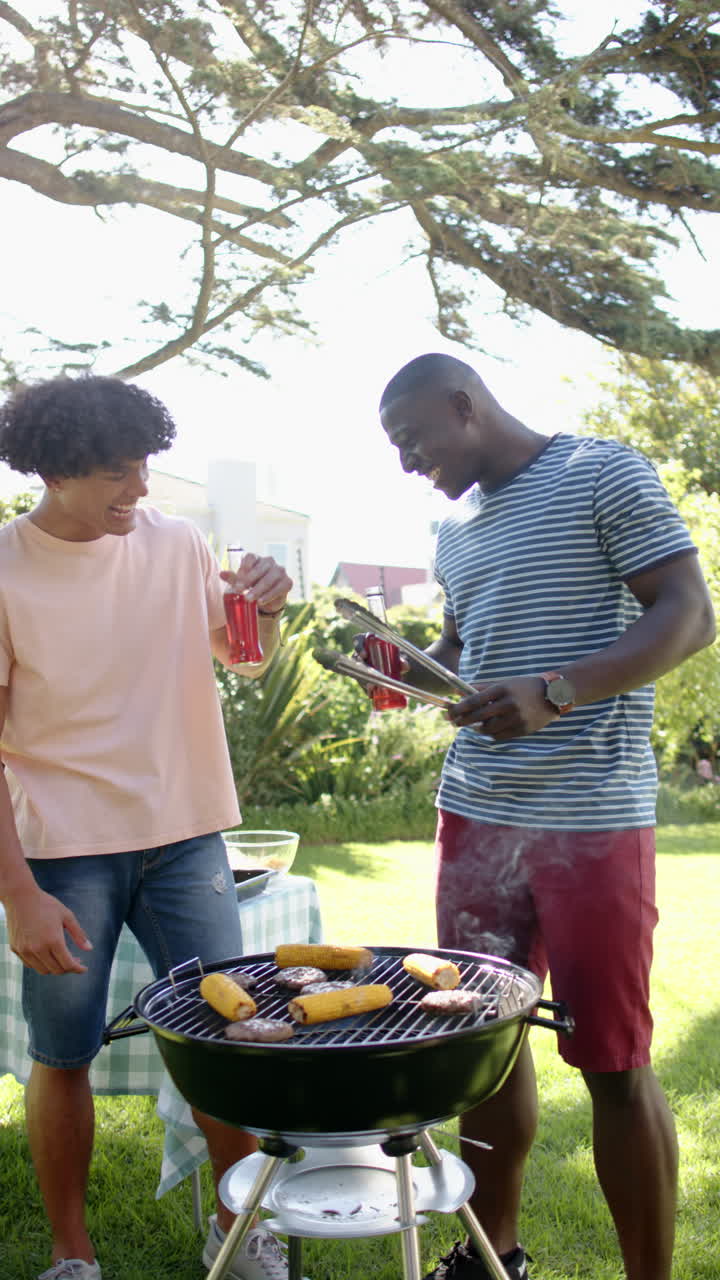 Vertical video: Friends enjoying barbecue outdoors, toasting with drinks and grilling food